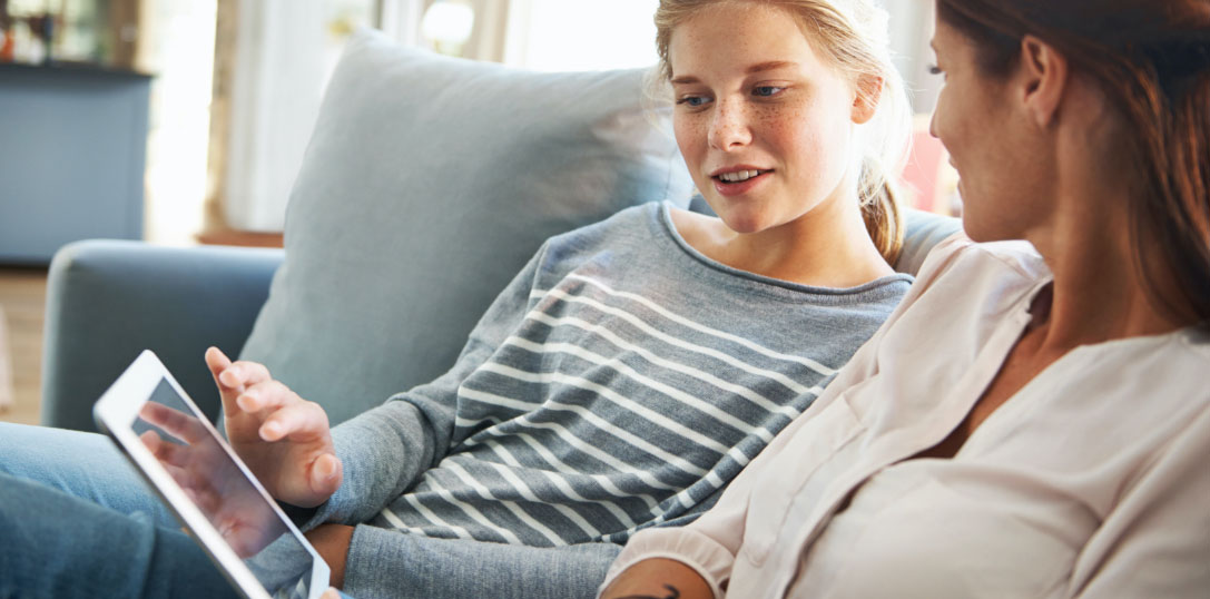 two woman sitting on a sofa looking at a tablet together